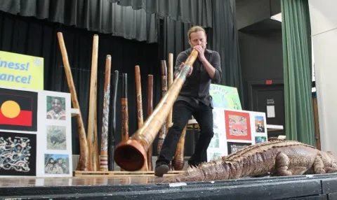 Cast member blowing didgeridoo instrument on stage